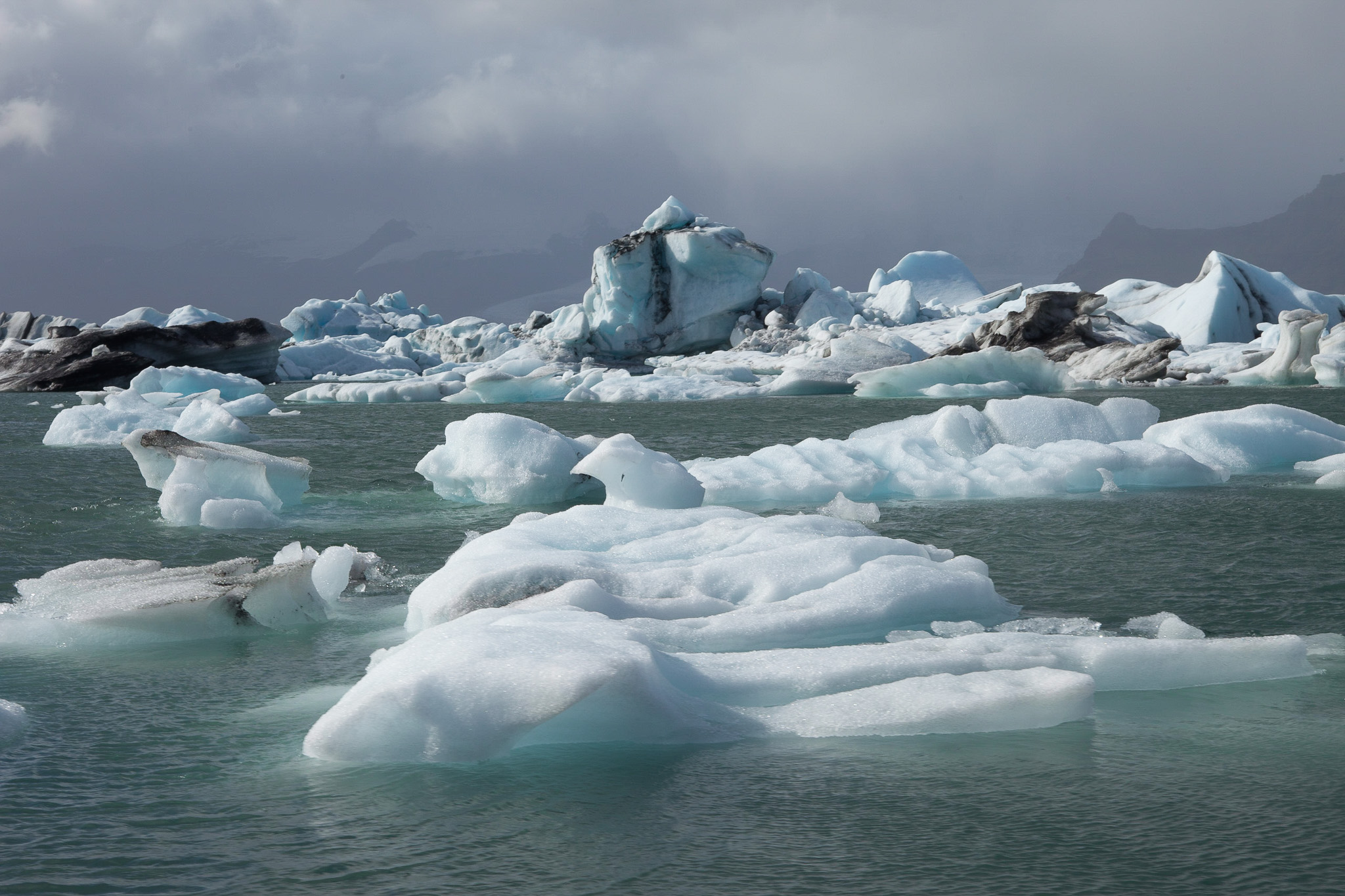 inúmeros icebergues flutuam no lago glaciar da Islândia. Uns têm a sua ponta pintada de preto devido às cinzas vulcânicas de erupções.